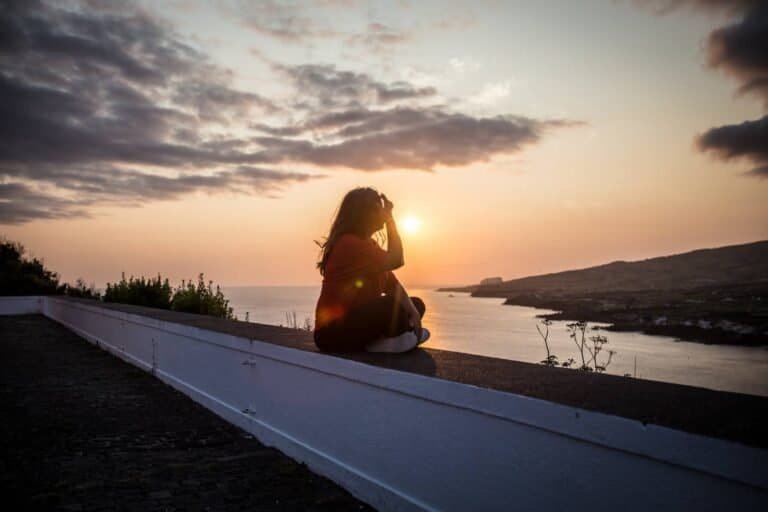 Woman sitting and watching sunset over Horta on Faial in the Azores, Portugal.