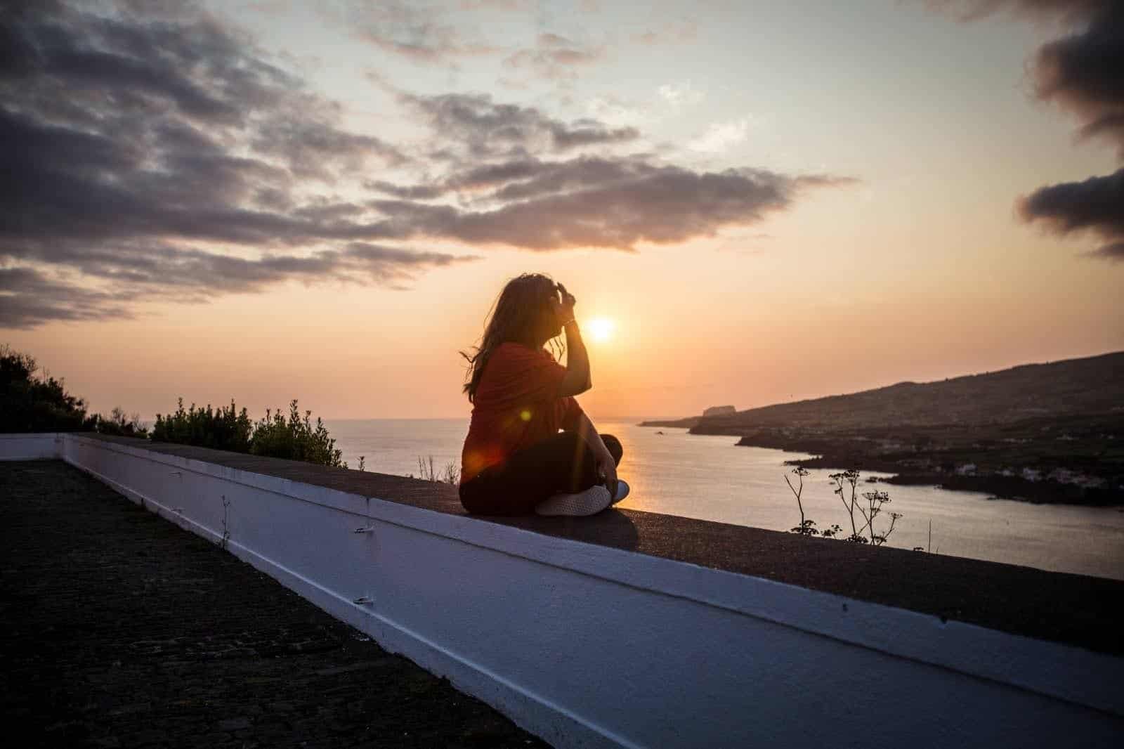 Woman sitting and watching sunset over Horta on Faial in the Azores, Portugal.