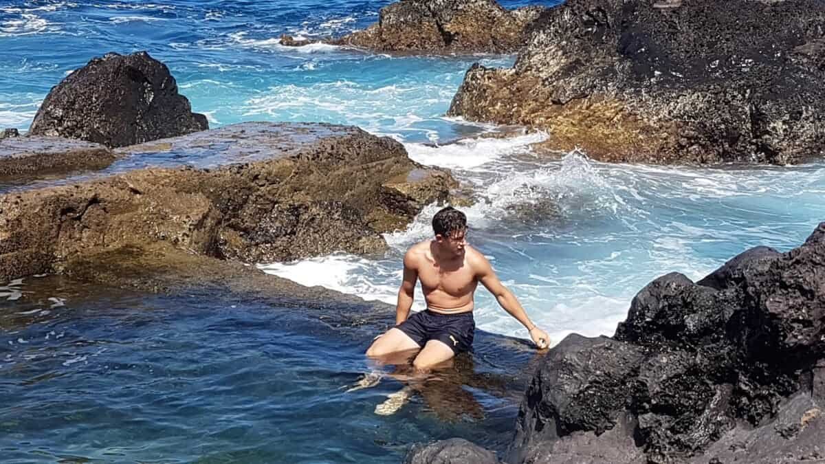 Young man relaxing in natural rock pool on Faial in the Azores, with ocean waves crashing around.