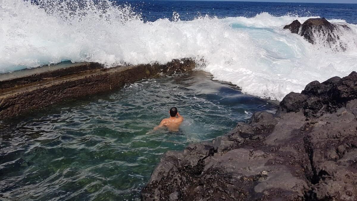 Person swimming in natural pool at Porto do Salão on Faial in the Azores, with ocean waves crashing nearby