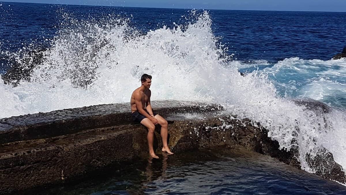 Giant ocean wave behind man sitting on wall in the Azores, Portugal