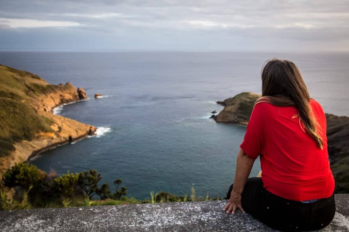 Woman in red shirt sitting on stone wall overlooking a bay on Faial in the Azores