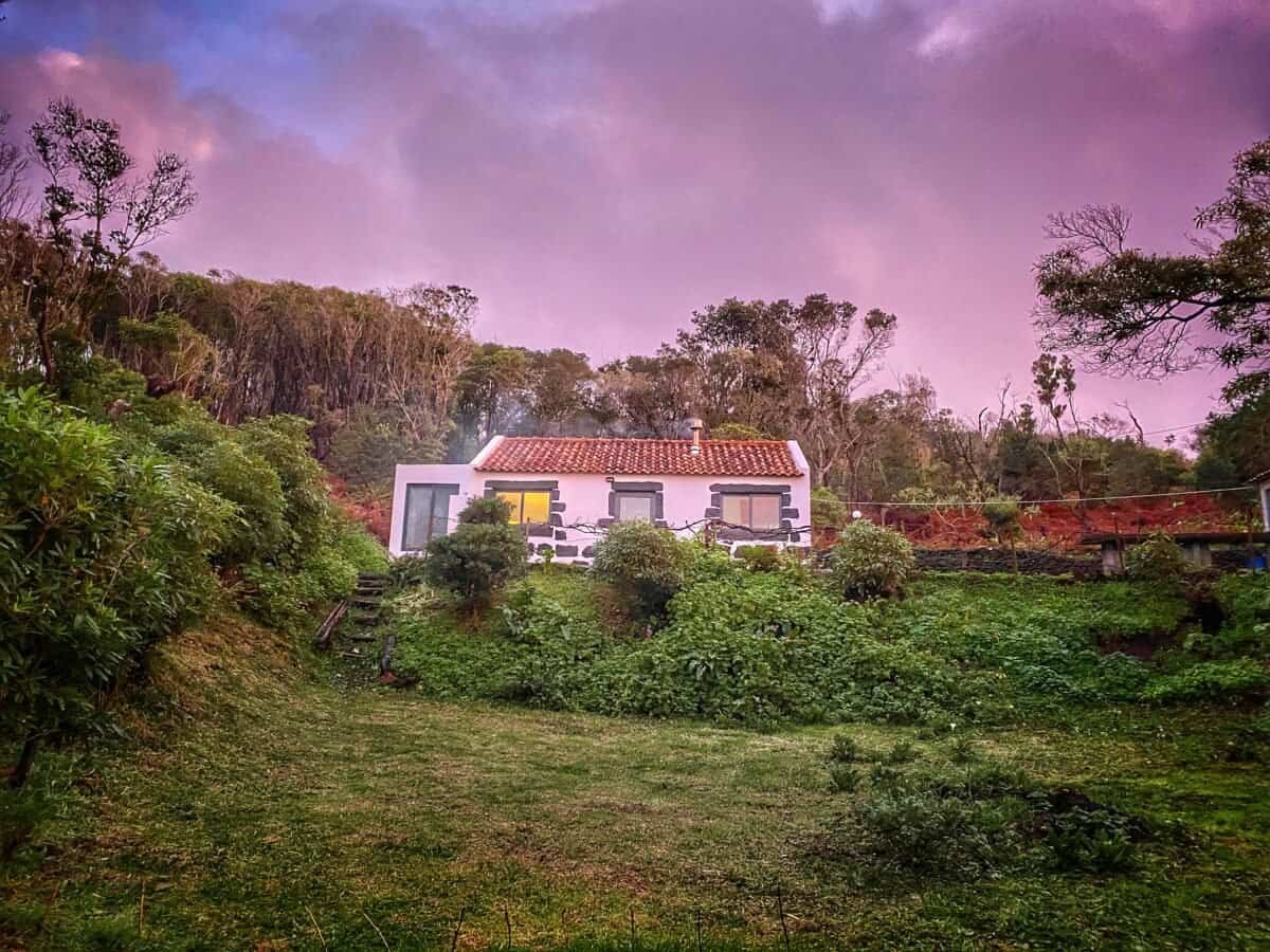 Small charming house on Faial in the Azores with lush garden and sunset background.