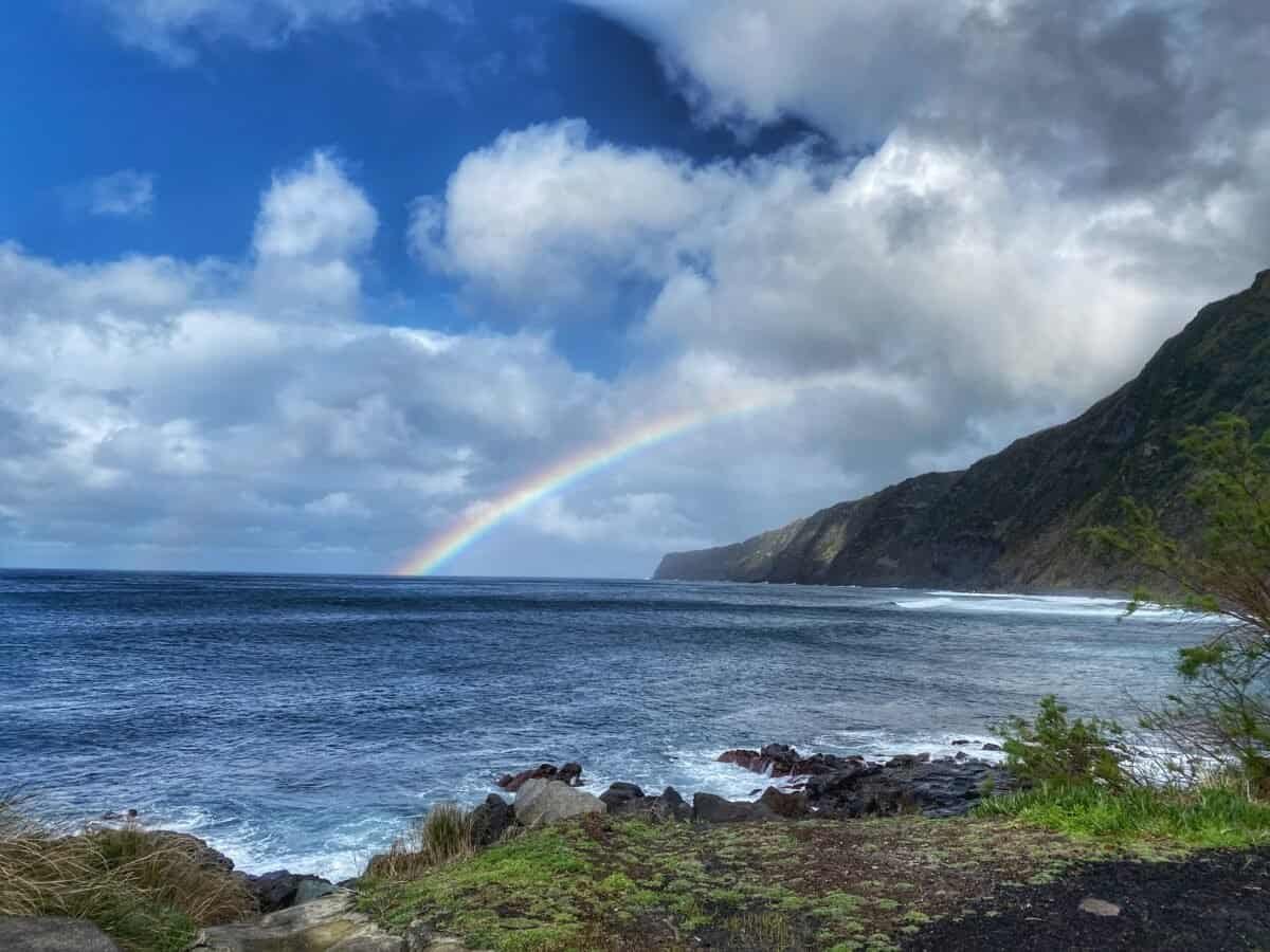 Rainbow over the beach at Fajã on Faial in the Azores, with lush green cliffs and ocean waves