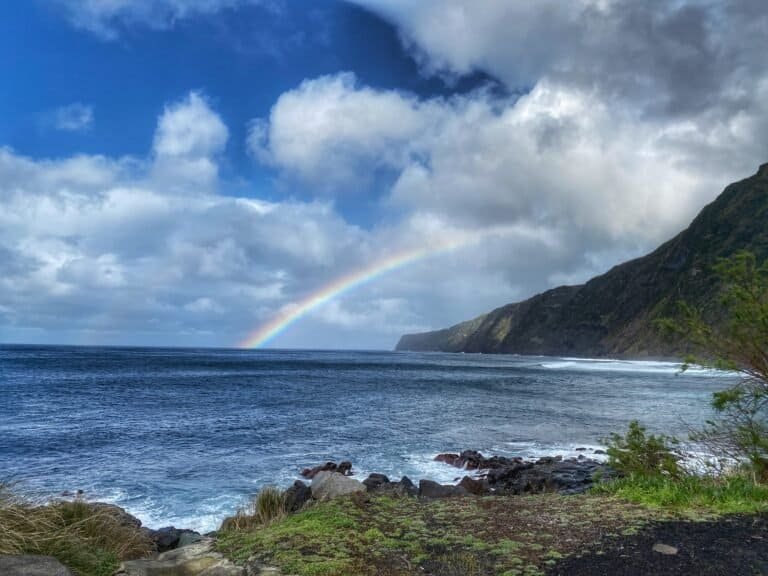 Rainbow over the beach at Fajã on Faial in the Azores, with lush green cliffs and ocean waves