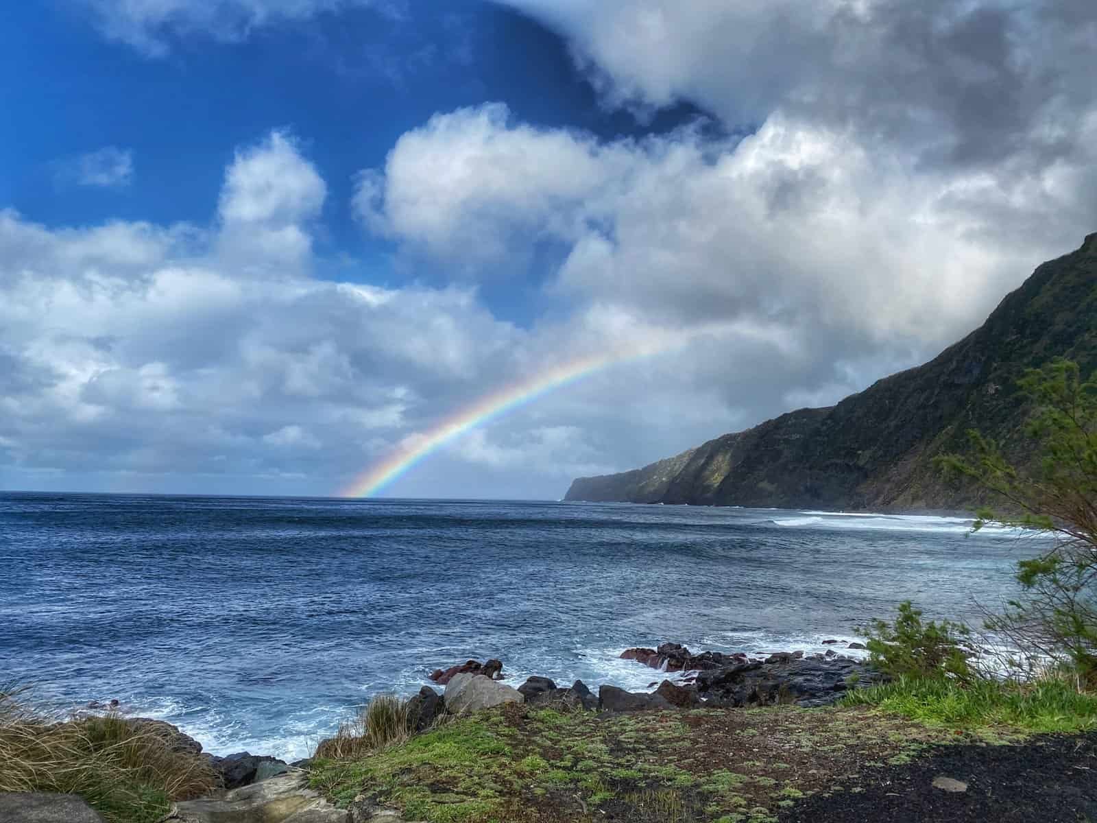 Rainbow over the beach at Fajã on Faial in the Azores, with lush green cliffs and ocean waves