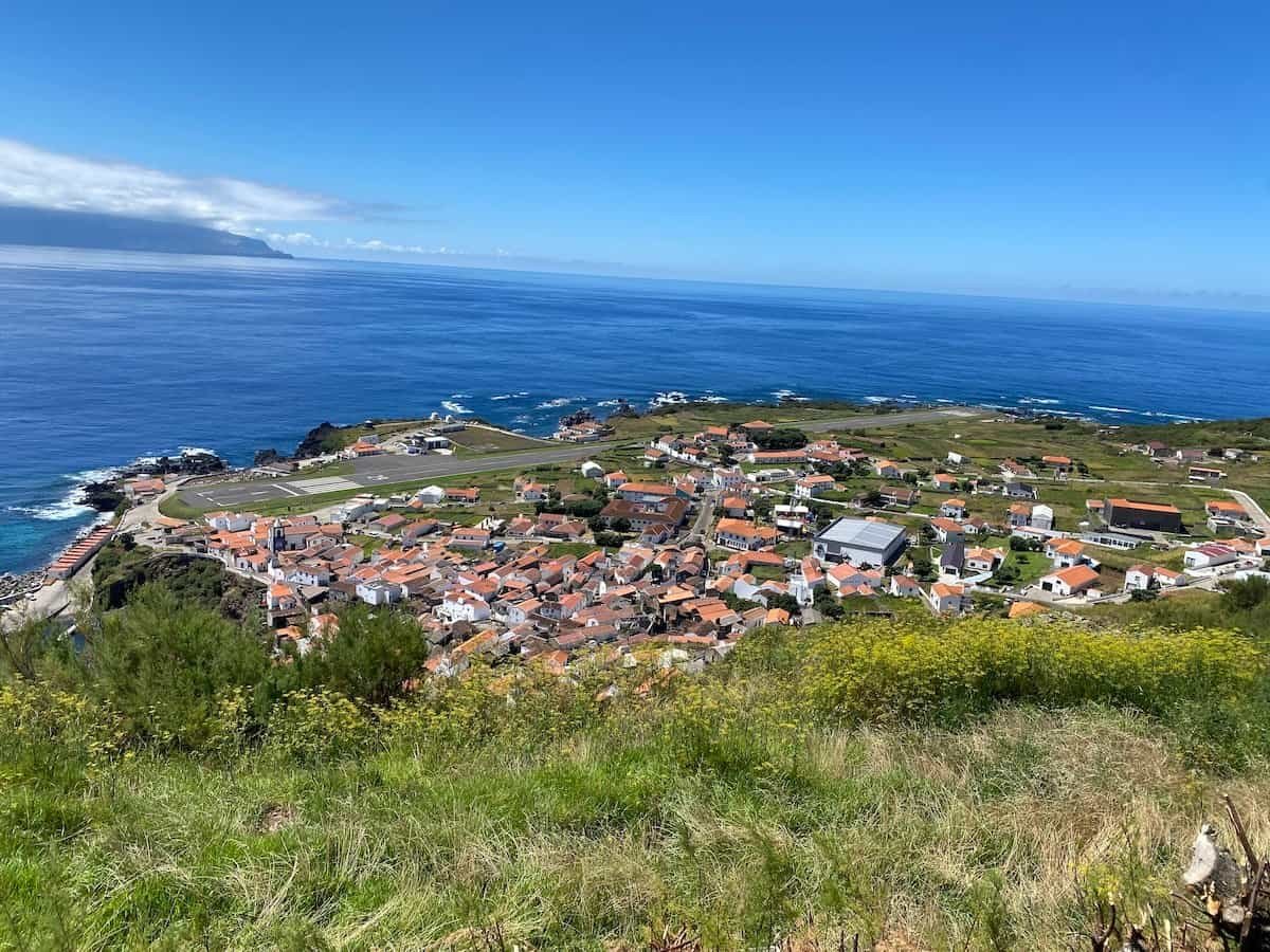 Aerial view of island village with white houses and tile roofs, surrounded by vast ocean