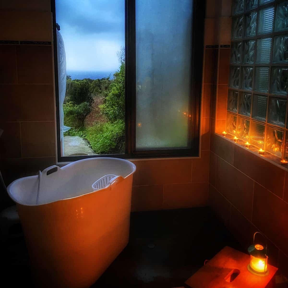 bathtub and candles near window with ocean view