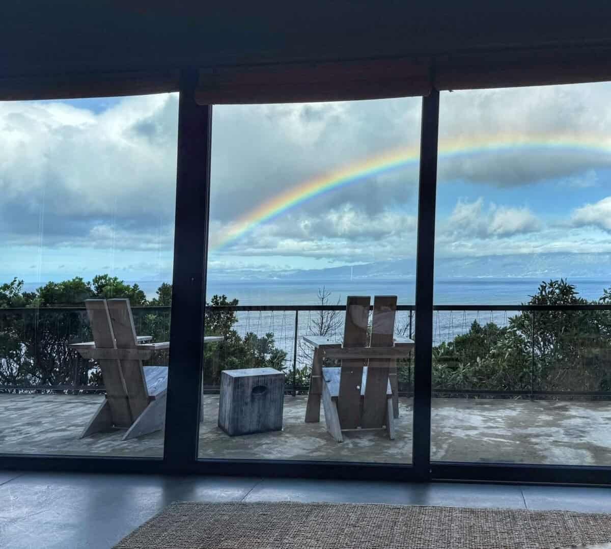 view through floor-to-ceiling windows of rainbow over ocean and distant São Jorge Island at Lava Homes on Pico Island