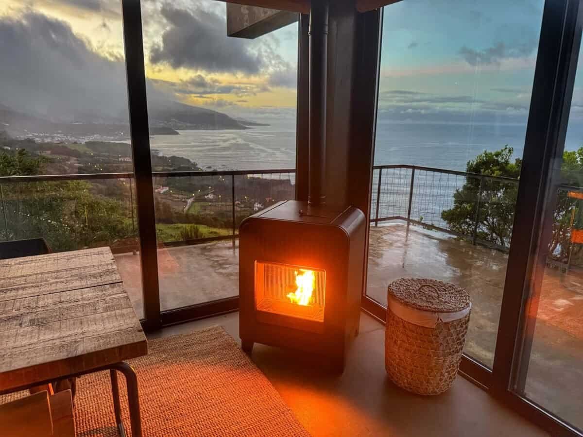 woodstove in corner of stone house with floor-to-ceiling windows overlooking ocean at Lava Homes on Pico Island
